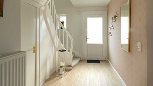 Un pasillo con una puerta blanca, una escalera y un espejo en la pared.