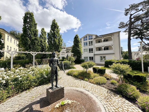 Uma estátua num jardim, com um edifício com a placa