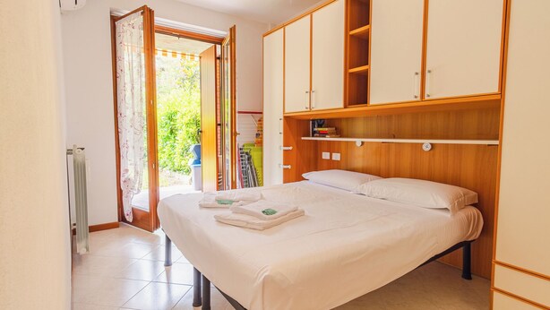 Ein Schlafzimmer mit einem Bett, einem Holzschrank und Blick ins Freie.