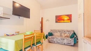 Ein gemütliches Zimmer mit Esstisch, Stühlen, einer Couch, einem Fernseher und einem Sonnenuntergangsbild.