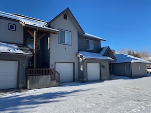 Une maison à deux étages avec un garage, une véranda et une allée recouverte de neige.