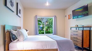 A bedroom with a large bed, a bedside table with a lamp, a dresser, and a window with curtains. - Della View 2BR condo - In the heart of Historic downtown Hailey! (Hailey)