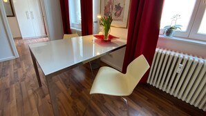 A modern room with a white table, a white chair, red curtains, a radiator, and a framed picture on the wall. - Excellently located 2-room apartment with balcony and high-speed internet in Mitte (Berlin)