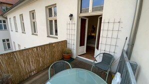 A small patio with a glass table and two chairs, a potted plant, and a wooden deck. - Excellently located 2-room apartment with balcony and high-speed internet in Mitte (Berlin)