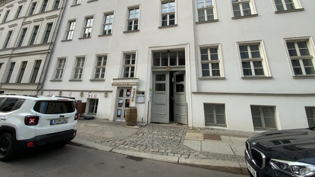 A white building with multiple windows and a door. There is a white SUV parked in front. - Excellently located 2-room apartment with balcony and high-speed internet in Mitte (Berlin)