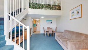 A two-story apartment with a dining area, a sofa, and a staircase.