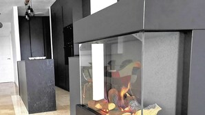Une cheminée moderne avec une façade en verre, entourée de murs en pierre noire, dans une pièce spacieuse dotée d’un sol carrelé.