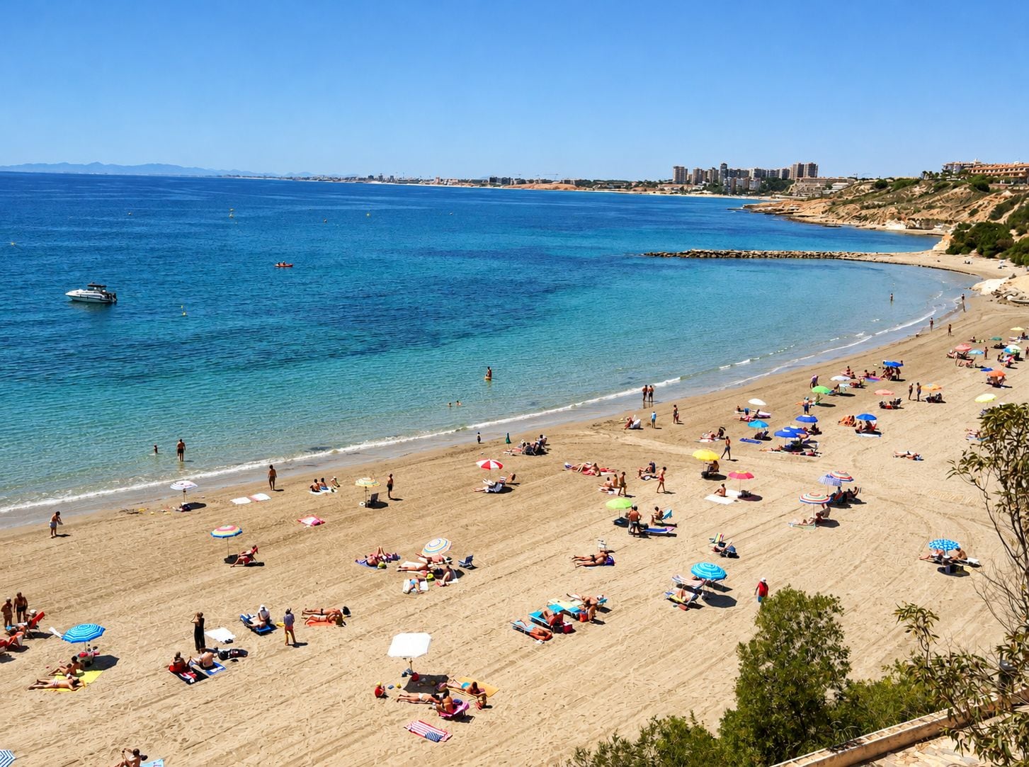 A beach with clear blue water, people sunbathing, and a boat in the distance.