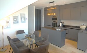 A modern kitchen with grey cabinets, a central island, and a dining area with a glass table and grey chairs. - Magnificent villa in Orihuela Costa close to everything with heated pool* (Orihuela)