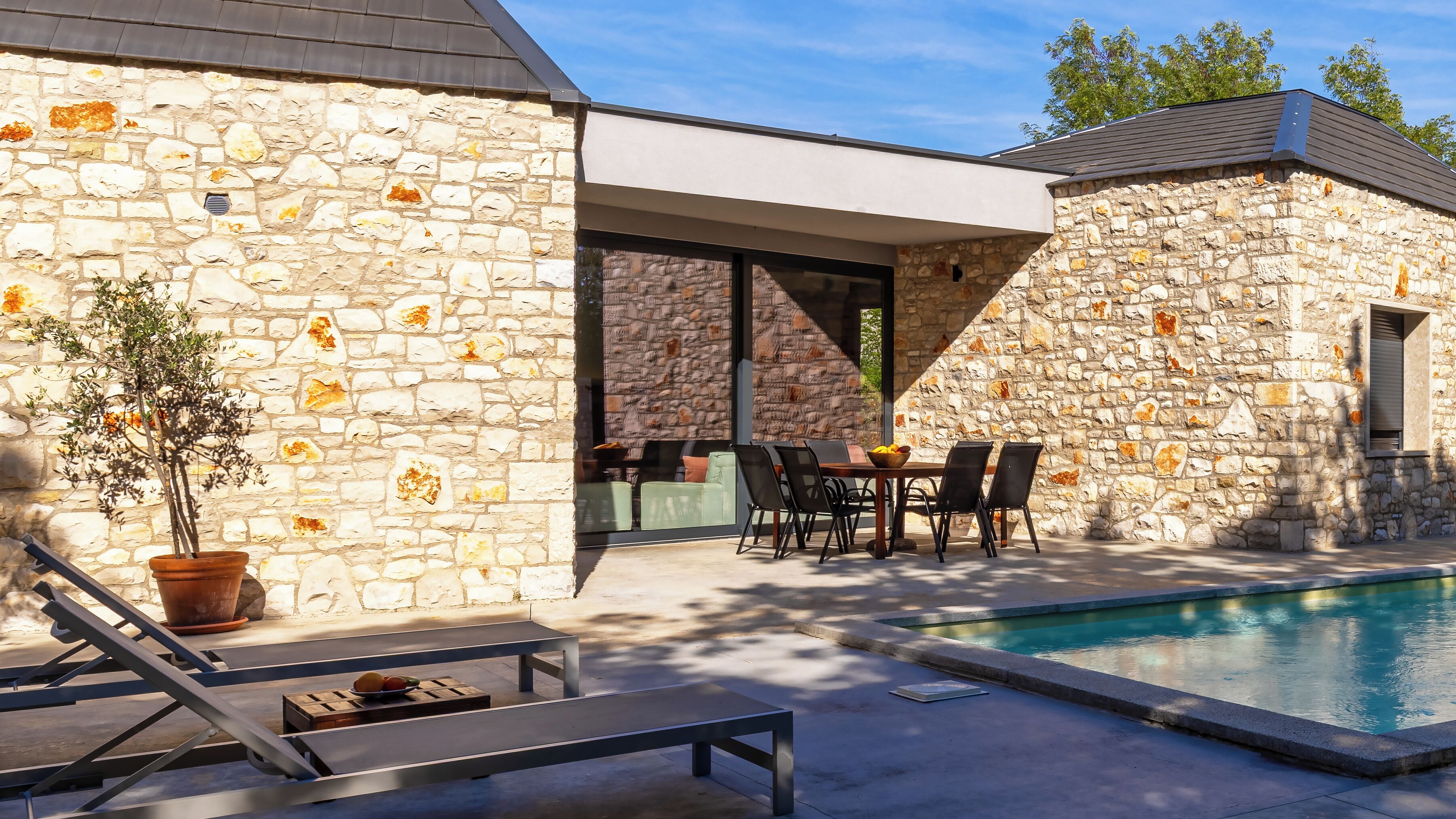 A stone building with a pool, outdoor seating, and a potted plant.