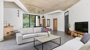 Ein modernes Wohnzimmer mit Sofa, Couchtisch und Fernseher. Es gibt eine Küchenzeile mit Spüle und Arbeitsplatte.