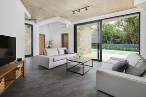 A modern living room with a large TV, two sofas, a coffee table, and a stone wall. - Unique Design Villa Doris (Umag)