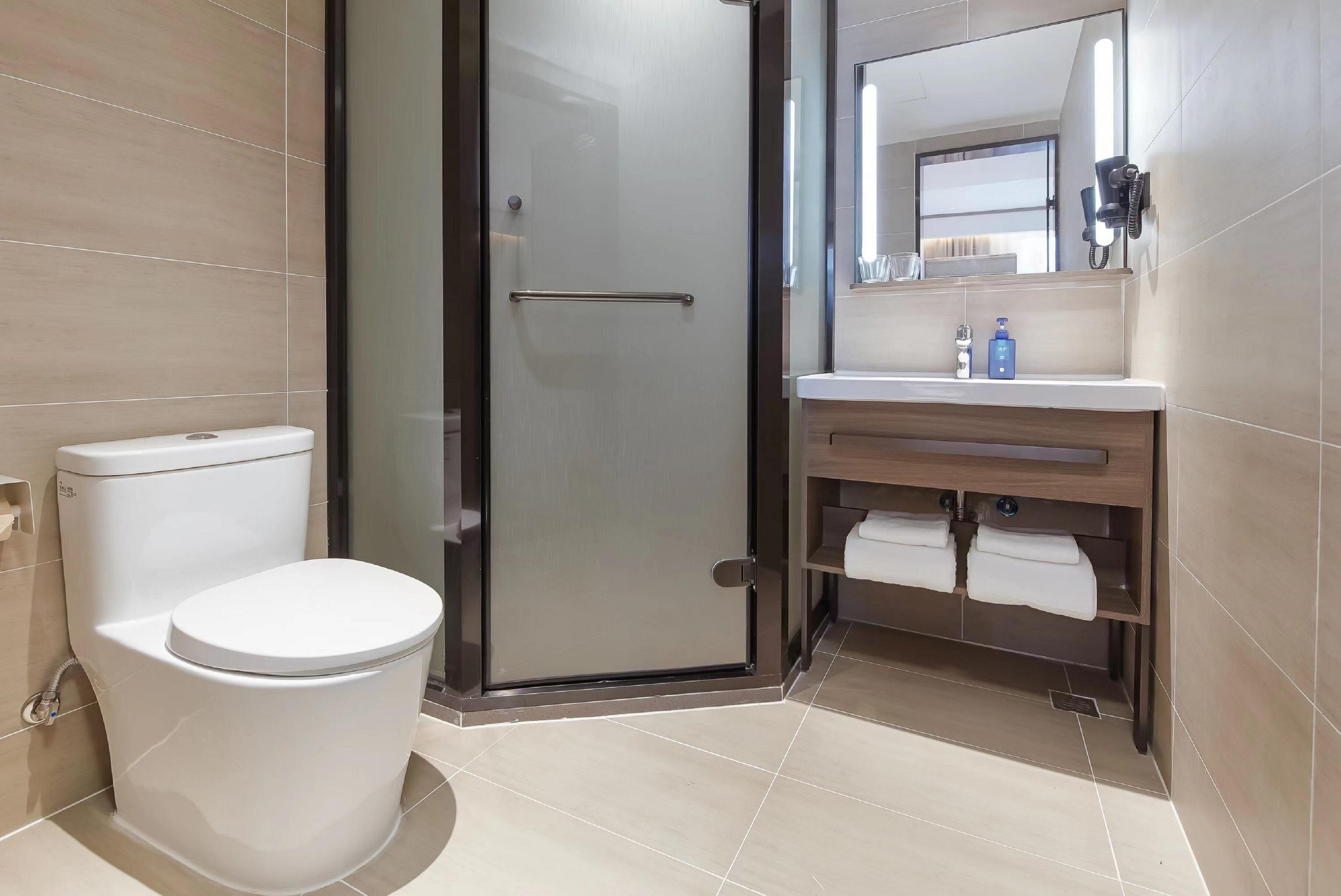 Un baño moderno con inodoro, cabina de ducha de vidrio, lavabo con espejo y toallero.