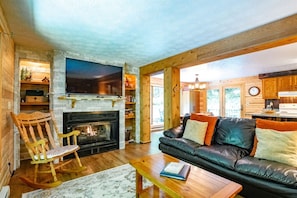 A cozy living room with a fireplace, a leather sofa, and a television. - Harvest Moon - Lake Access, Wooded Lot, Hot Tub! (Davis)