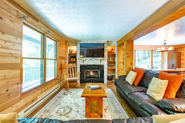 A cozy log cabin interior with a fireplace, leather sofa, and wooden walls.
