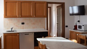 Una cocina con armarios de madera, lavavajillas, microondas y televisor montado en la pared.