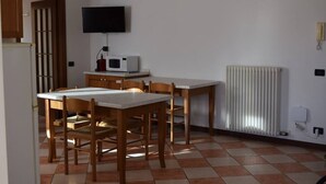 Una pequeña cocina equipada con microondas, una mesa, sillas, un televisor y un radiador.
