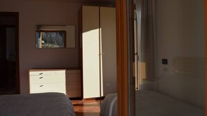 Un dormitorio con cama, cómoda, armario y ventana con vistas a árboles.