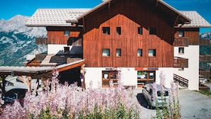 Un bâtiment en bois doté de nombreuses fenêtres et de balcons, un magasin de ski et un parking avec des voitures.