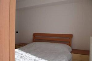 Un lit simple avec une tête de lit en bois, dans une pièce aux murs unis et agrémentée d’une petite table de chevet.