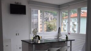 Una cocina moderna con una isla central, taburetes blancos, un televisor de pantalla plana y ventanas amplias con vista a la ciudad.