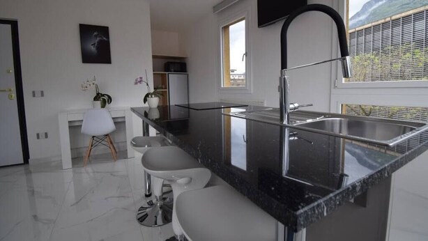 Una cocina moderna con encimera negra, pileta de acero inoxidable y ventana con vistas a montañas.