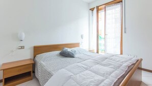 Een slaapkamer met een houten bed, een nachtkastje, een raam met uitzicht en een wandlamp.