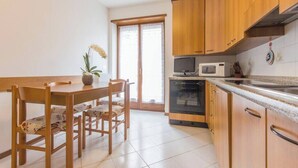 Een keuken met houten kastjes, een magnetron, een oven en een eettafel met stoelen.