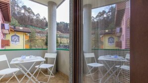 Een balkon met witte stoelen en een tafel, met uitzicht op een groen landschap met gebouwen.