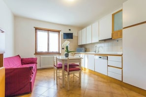 Ein kompakter Wohnbereich mit Küchenzeile, einem Essbereich mit Tisch und Stühlen, einer Couch und einem Fenster mit Jalousien.