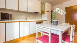 A compact kitchen with white cabinets, a microwave, a sink, and a dining area with a white table and chairs. - Family-Friendly Apartment Near Terme Comano (Ponte Arche)