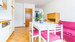 A compact living space with a kitchenette, a dining table with chairs, a sofa, and a potted plant. - Family-Friendly Apartment Near Terme Comano (Ponte Arche)