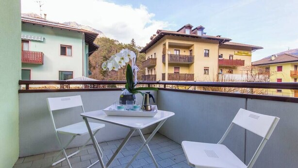 Un balcon avec deux chaises blanches, une petite table sur laquelle se trouve un plateau avec divers objets, et une orchidée en pot.