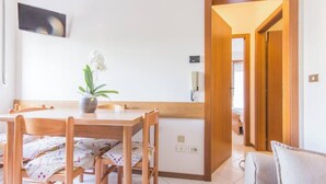 A dining area with a wooden table and chairs, a vase with an orchid, and a kitchen area visible through an open doorway.