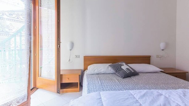 A bedroom with a bed, a nightstand, a bedside table, a lamp, and a window with a view.