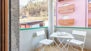 A balcony with a table and chairs, a view of a building with balconies, and a green railing.