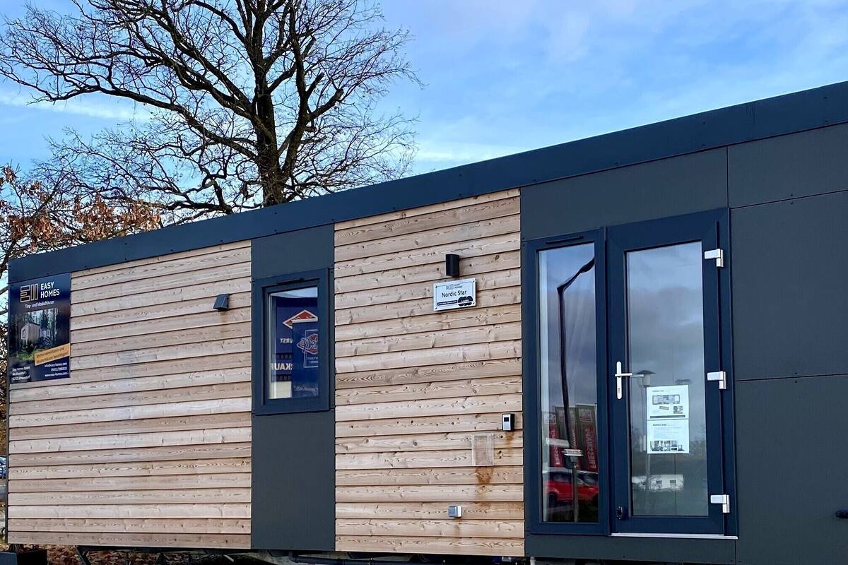 Una cabaña moderna y compacta con revestimiento de madera y detalles oscuros, con ventanas amplias y una puerta visible.