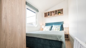 A bedroom with a bed, bedside tables, a window, and a shelf with decorative items.