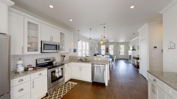 A modern kitchen with white cabinetry, stainless steel appliances, and a long countertop.