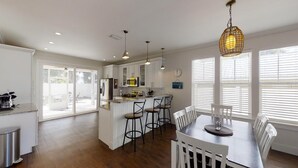 A modern kitchen with white cabinets, a central island with bar stools, and a dining area with a table and chairs.