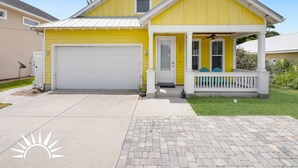 A yellow single-story house with a white garage door, a front porch with a white railing, and a small front yard.