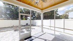 A covered patio with a wooden ceiling, glass doors, and a white fence.
