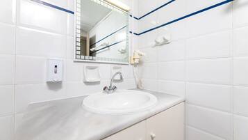 A bathroom with white tiles, a sink, a mirror, a hand dryer, and a soap dispenser.