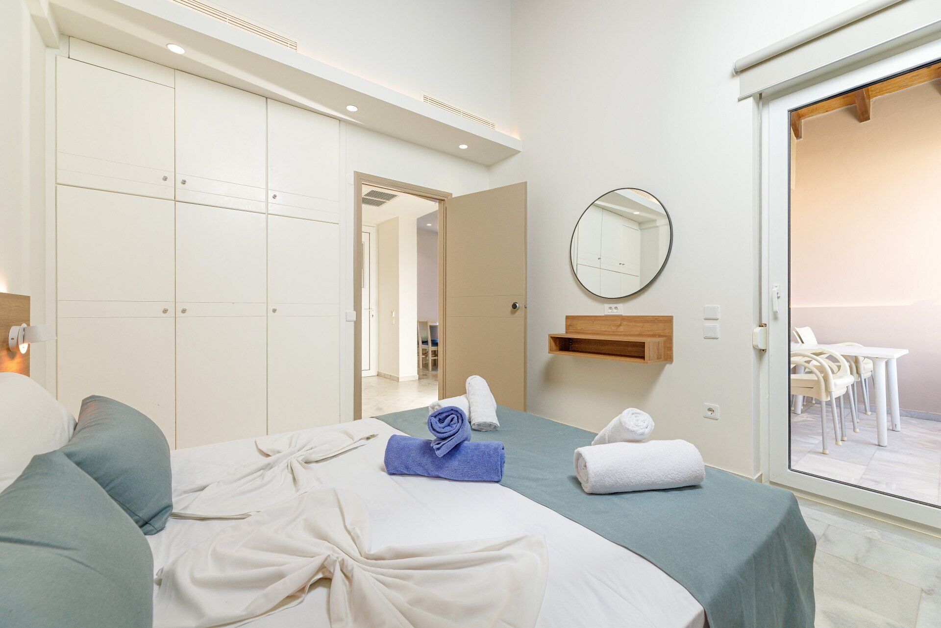 A hotel room with a bed, a mirror, a small table, and a view through a glass door.