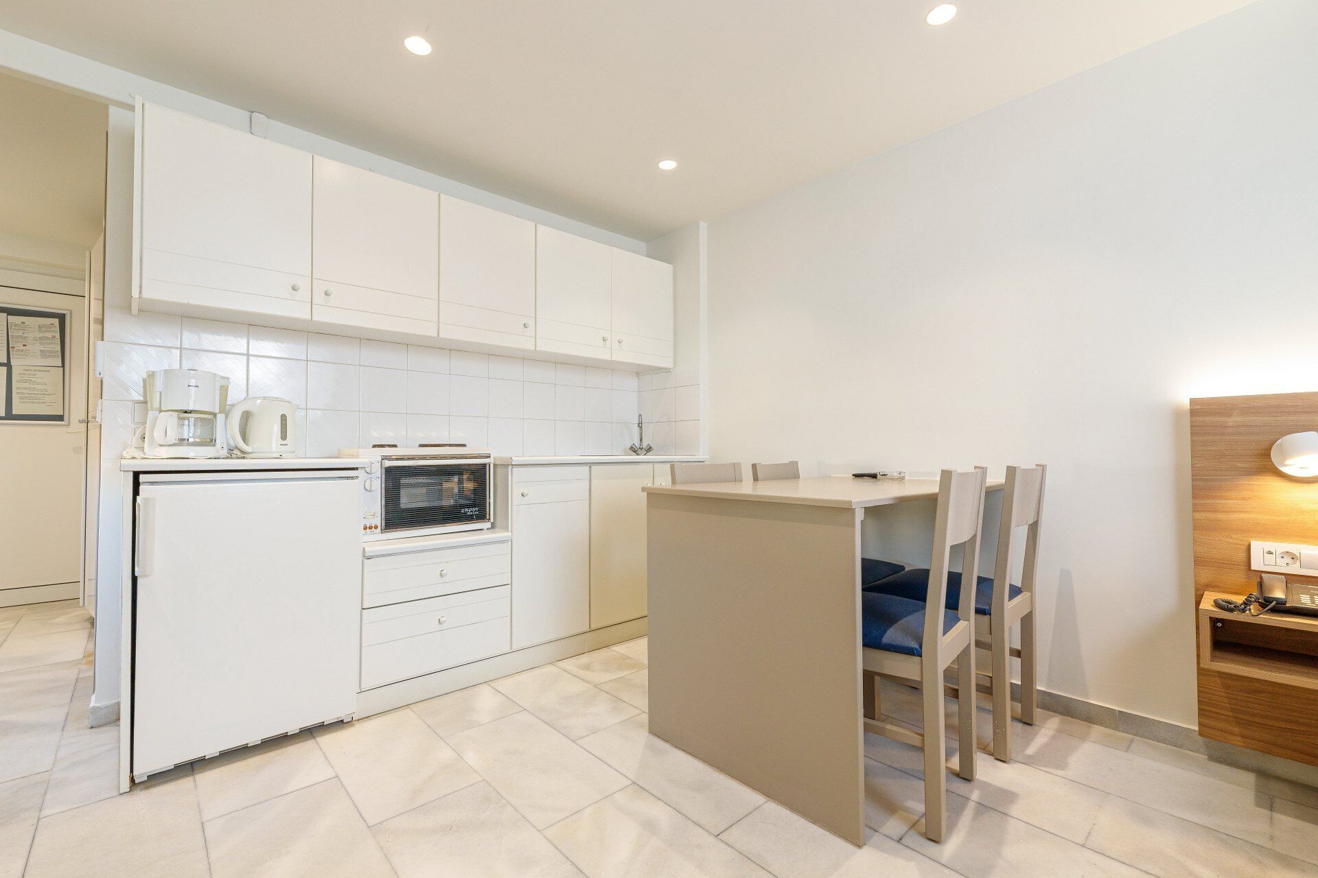 A modern kitchen with white cabinets, a coffee maker, an oven, and a small dining area with chairs.