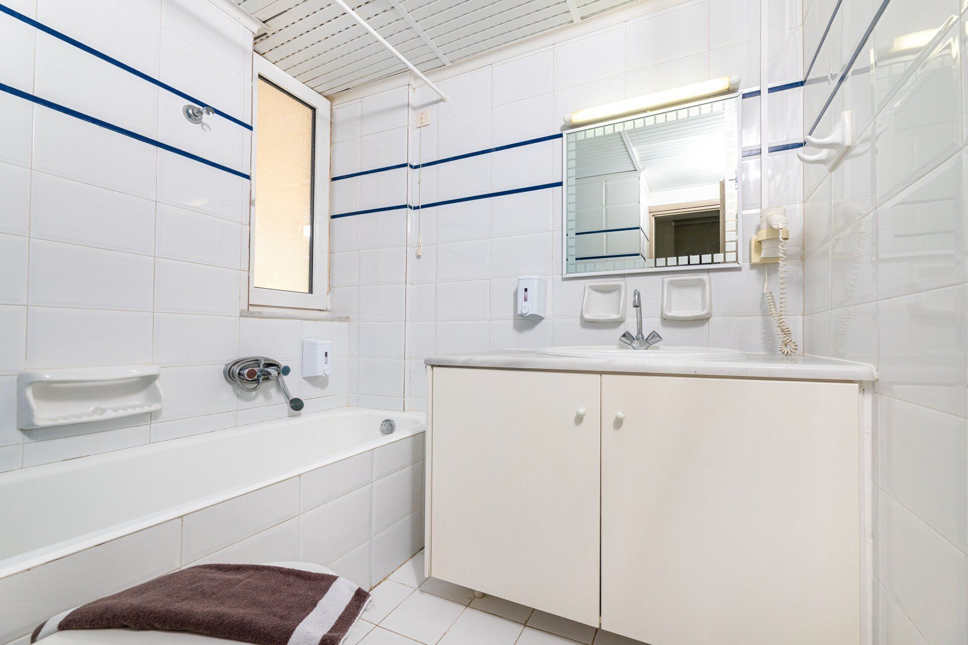 Een moderne badkamer met witte tegels, een badkuip, een wastafel met spiegel en een telefoon.
