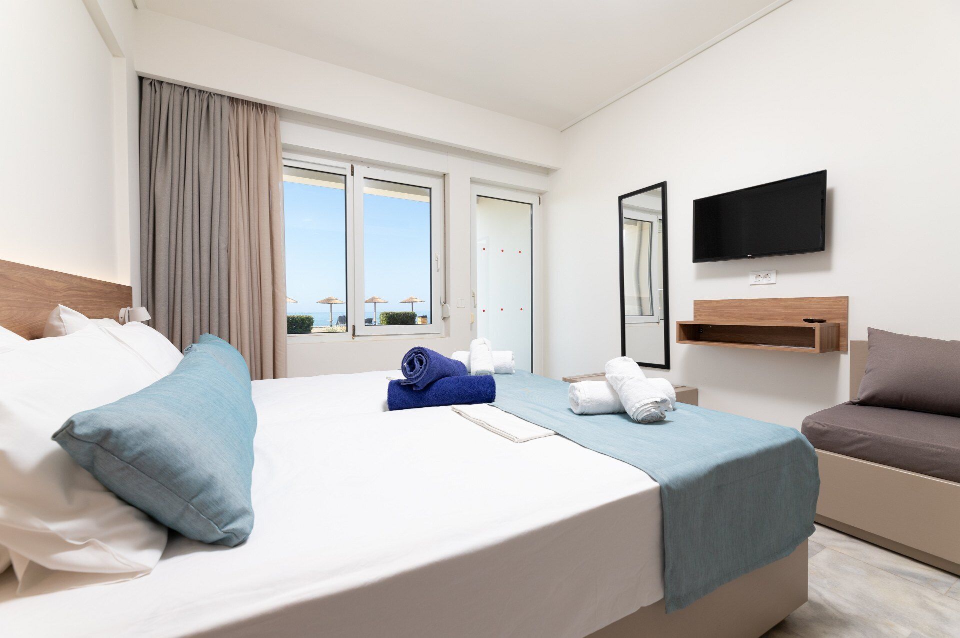 Habitación de hotel con cama, televisión, escritorio y vista a la playa.