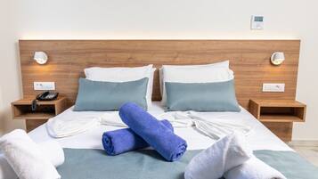 Habitación de hotel con cabecera de madera, dos mesitas de noche, un teléfono y un termostato digital.