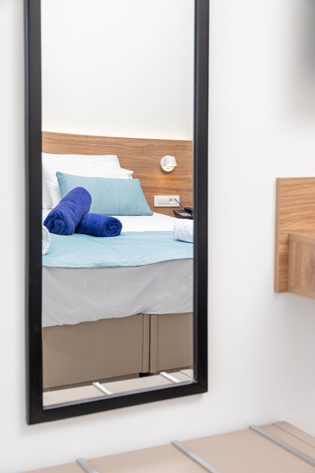 A hotel room with a bed, a wall-mounted light, and a wooden panel on the wall.