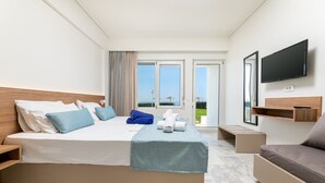 Habitación de hotel moderna con una cama grande, un sofá, un televisor y un balcón con vista al mar.